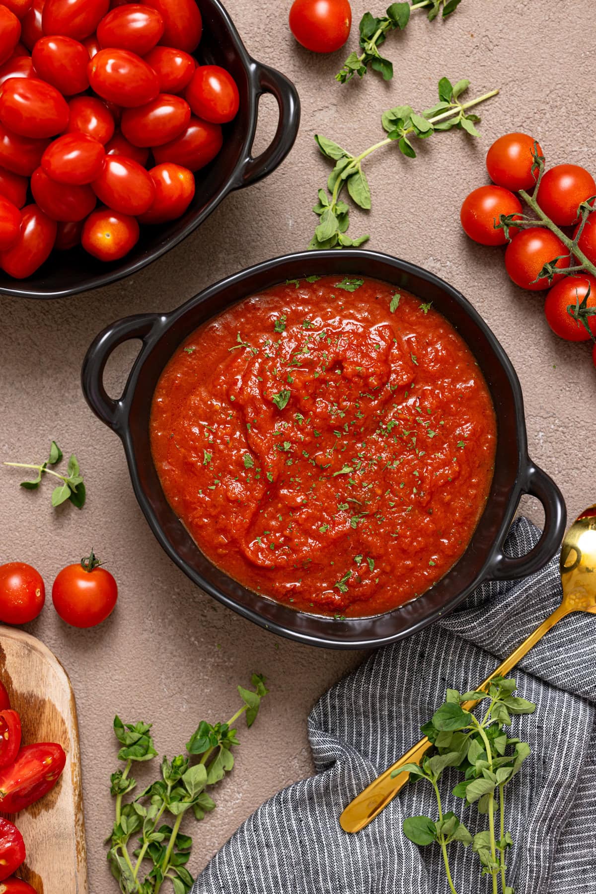 Tomato sauce in a black bowl with tomatoes and herbs.