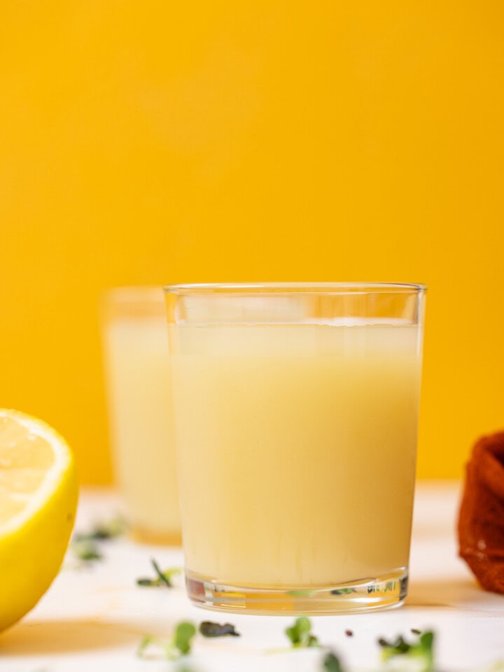 Two glasses of lemon juice with halves of lemons.