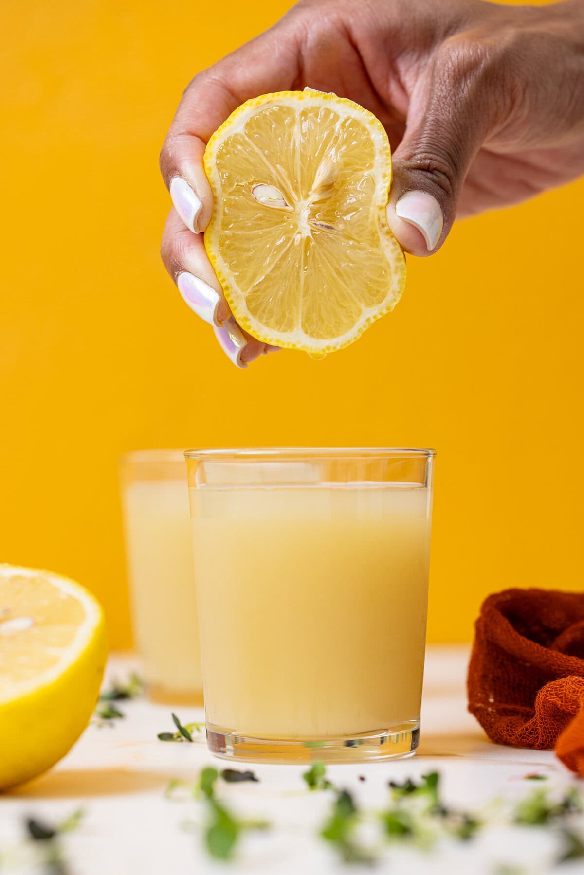 Two glasses of lemon juice with a lemon being held and squeezed.