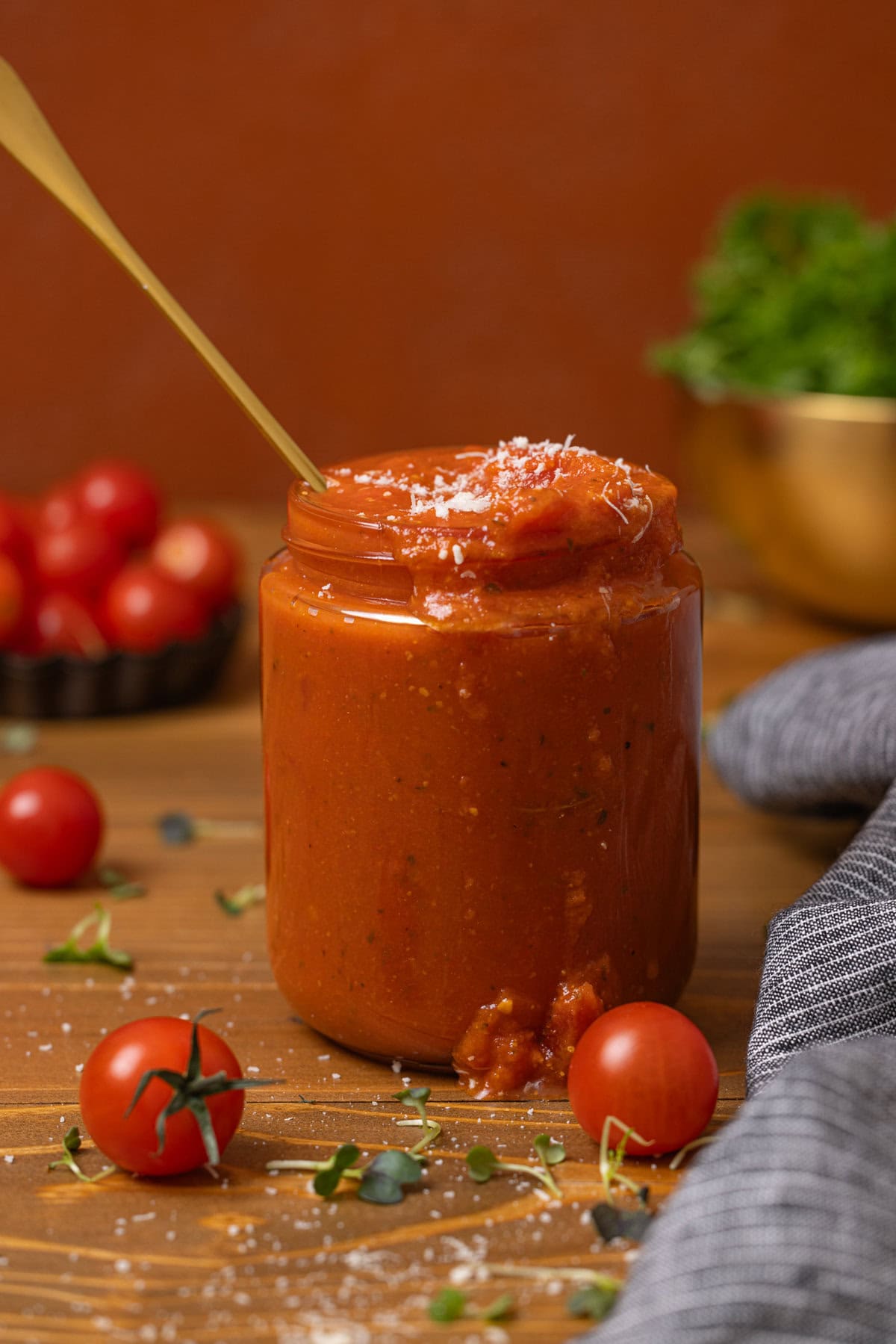 Vodka sauce in a jar with a spoon and tomatoes.