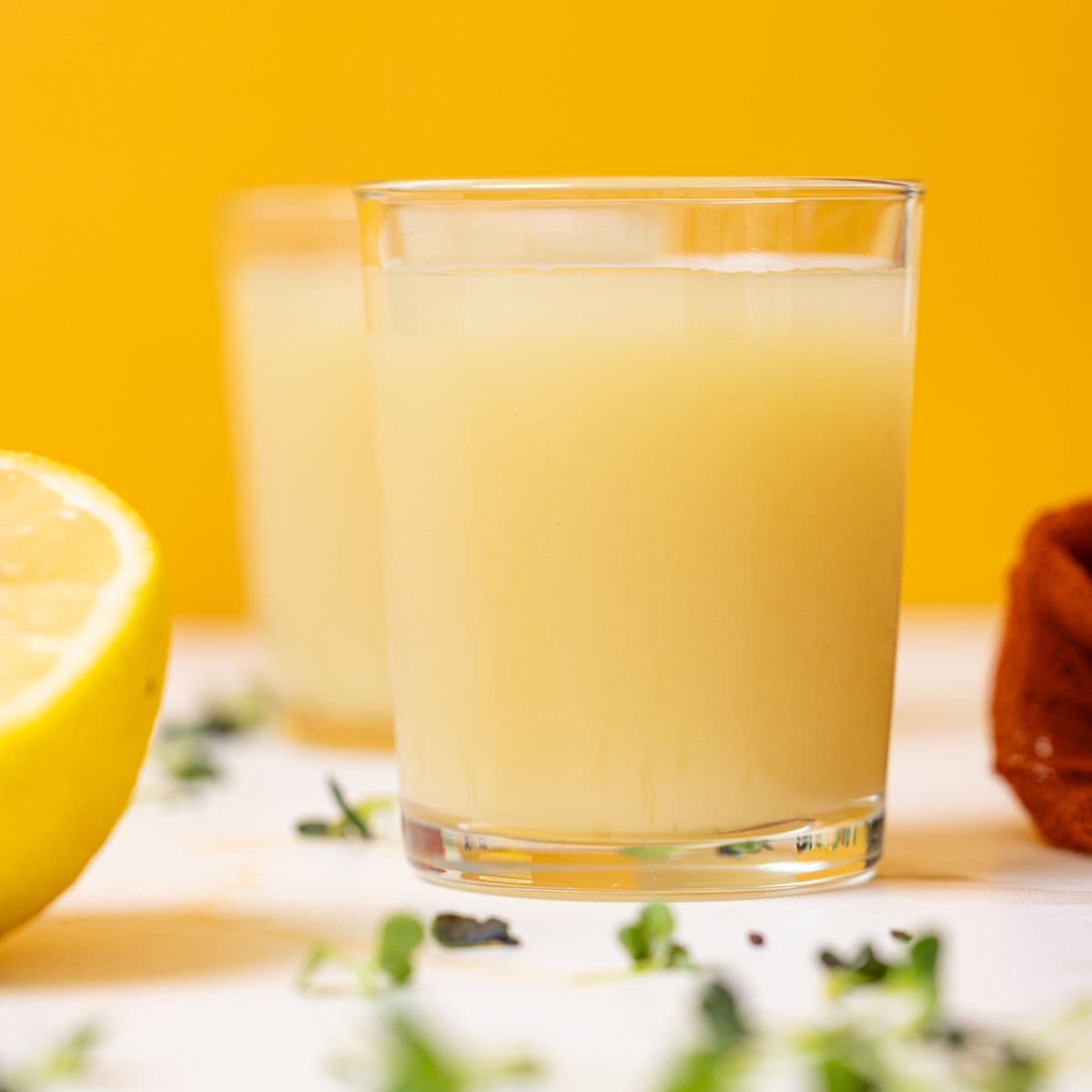 Two glasses of lemon juice with halves of lemons.