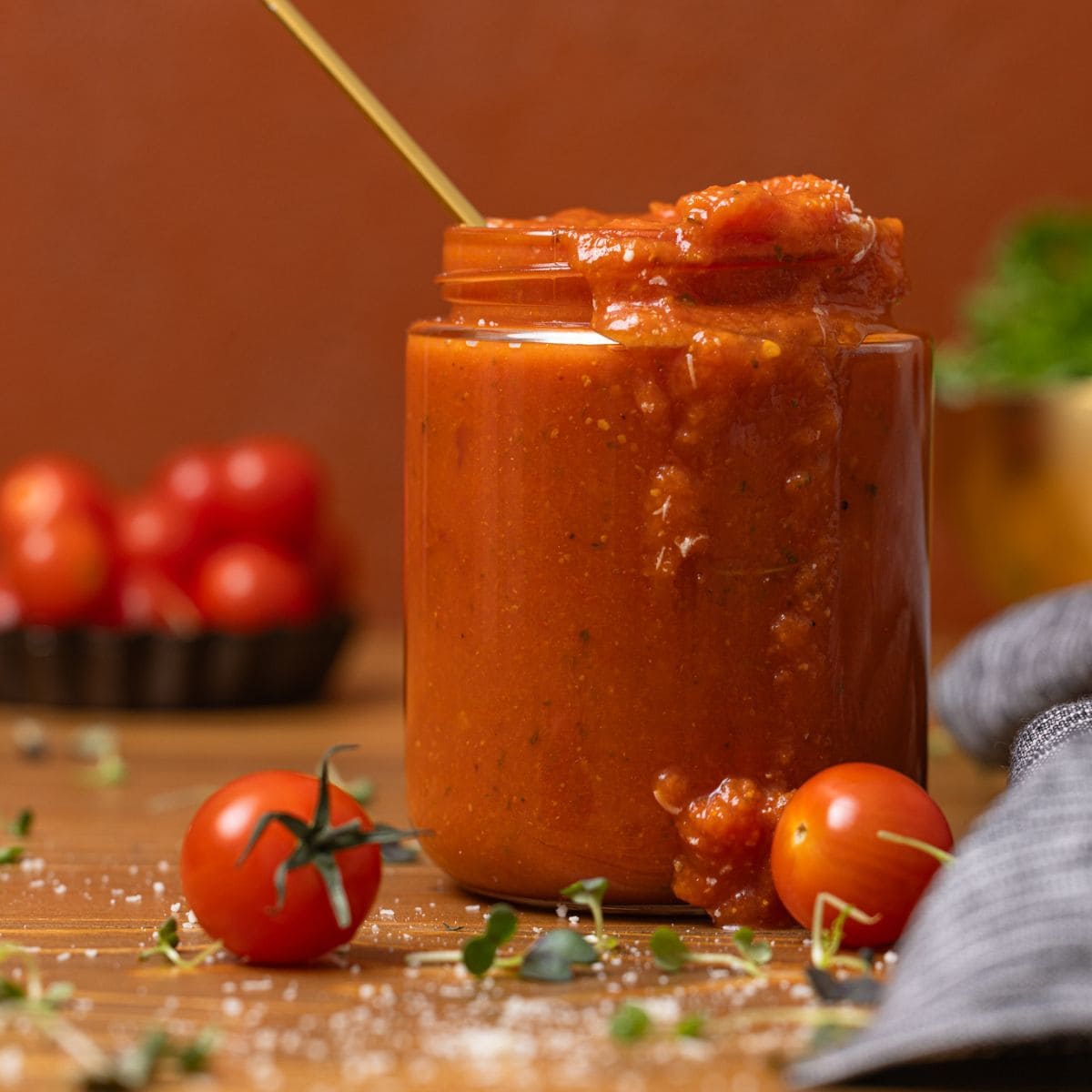 Vodka sauce in a jar with a spoon on a brown wood table with tomatoes.