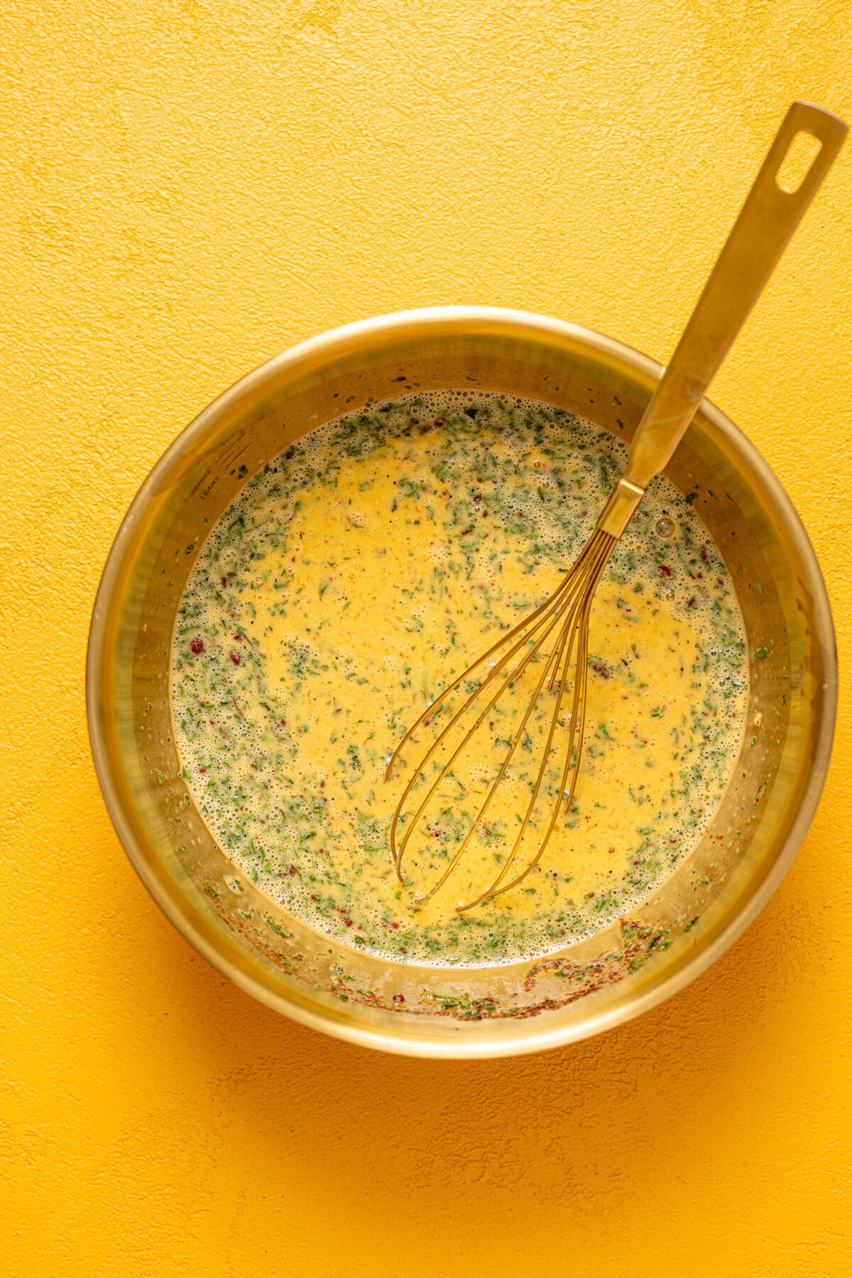 Egg mixture in a gold bowl with a whisk.