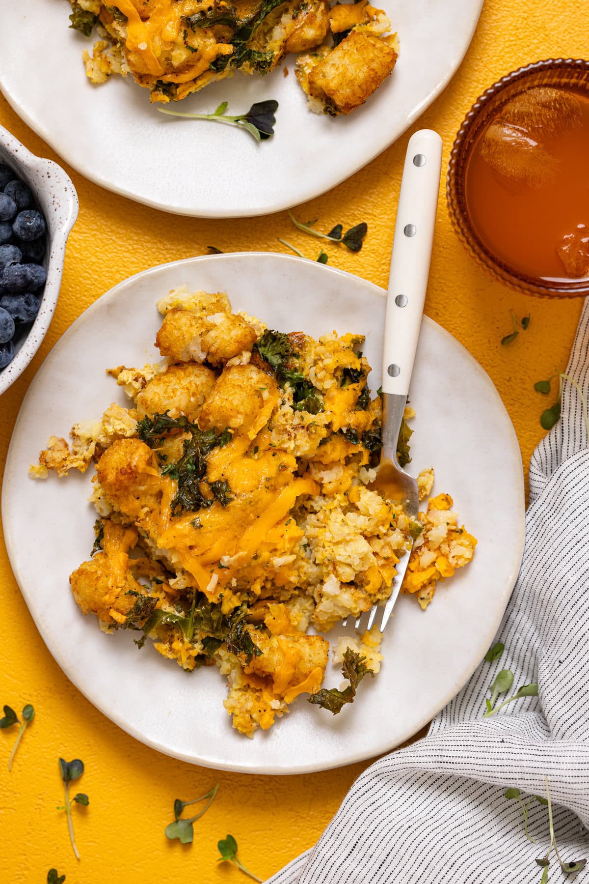 Two plates of baked tater tot casserole with a fork and drink.