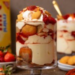 Two trifle bowls of strawberry banana puddings with a box of nilla wafers and strawberries in the background.