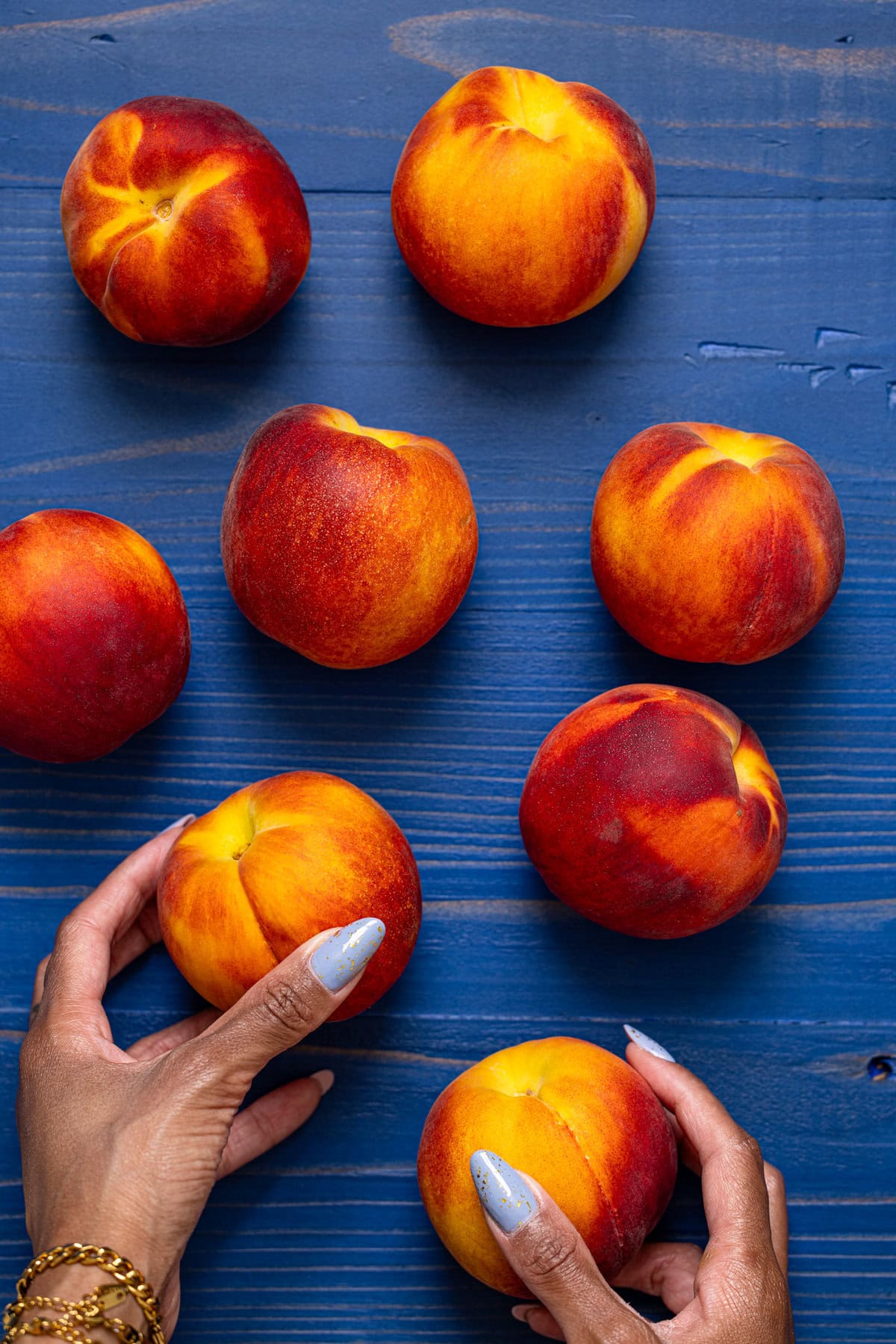 Peaches being held with hands on a blue wood table.