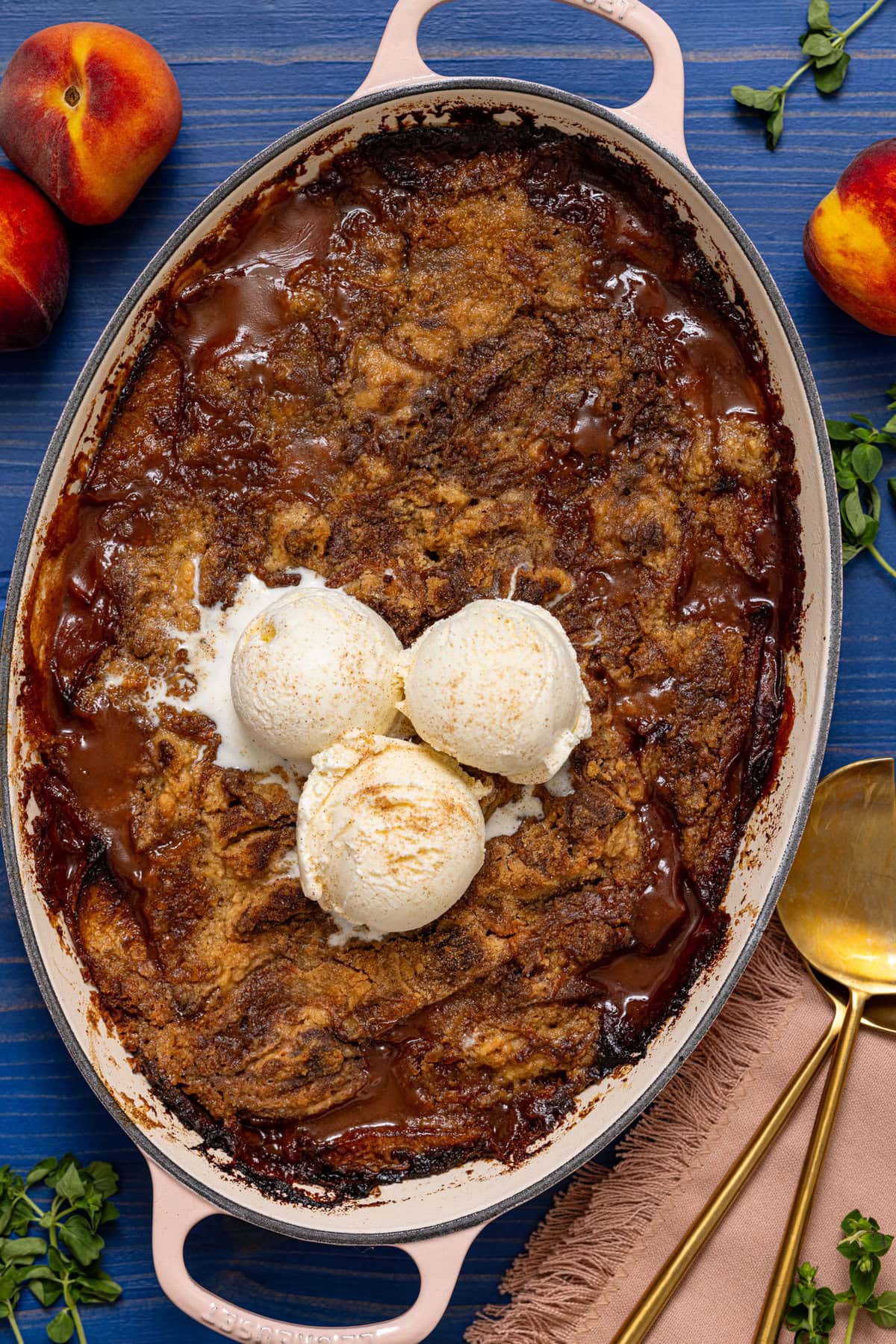 Baked peach dump cake in a baking dish with serving spoons and peaches.