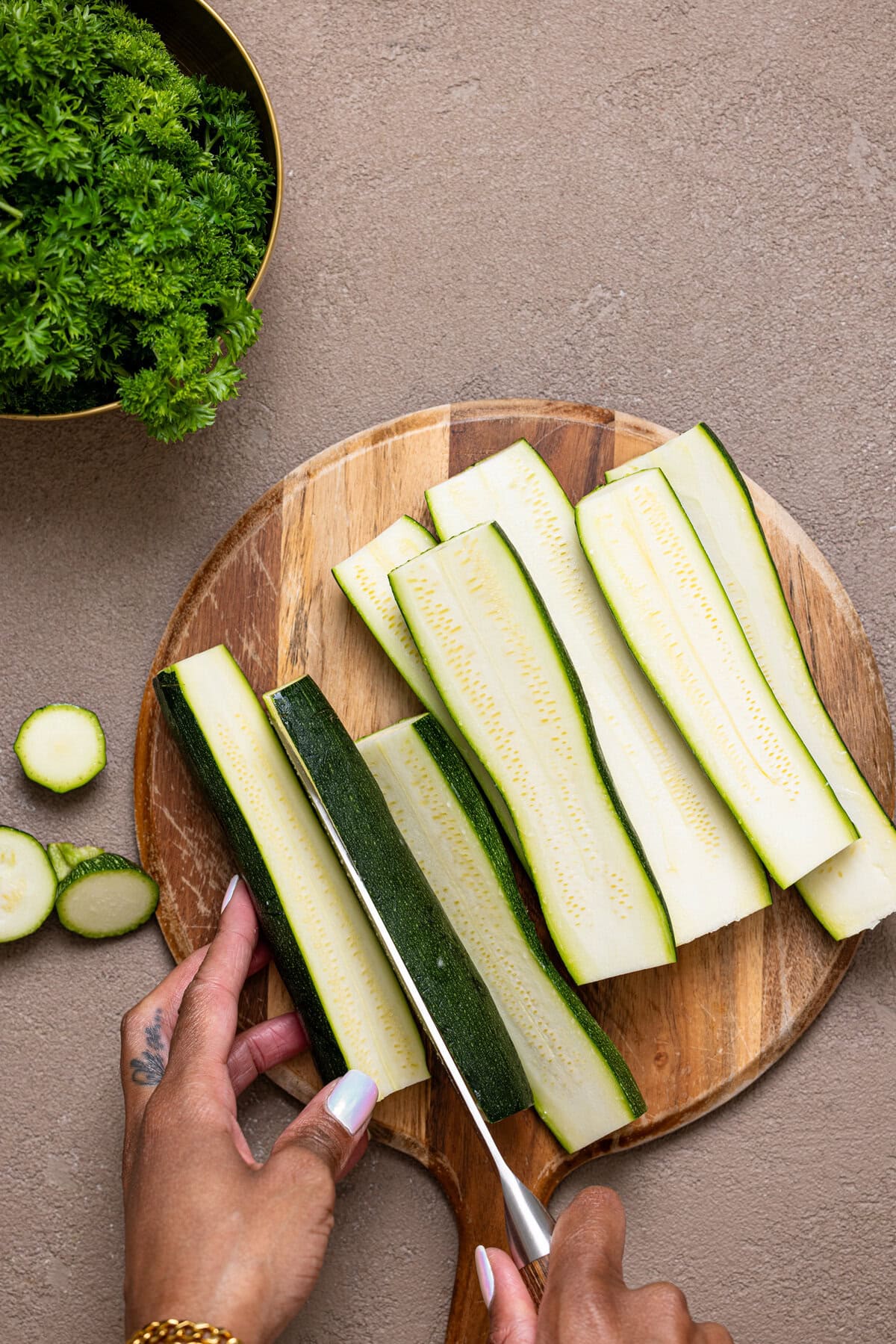 Zucchini being chopped on a cutting board with a knife. 