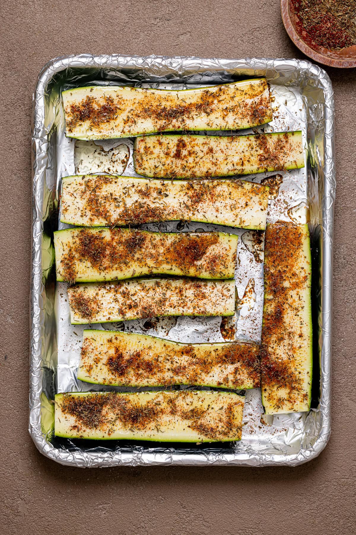 Sliced zucchini on a baking sheet with foil paper, lined and seasoned. 