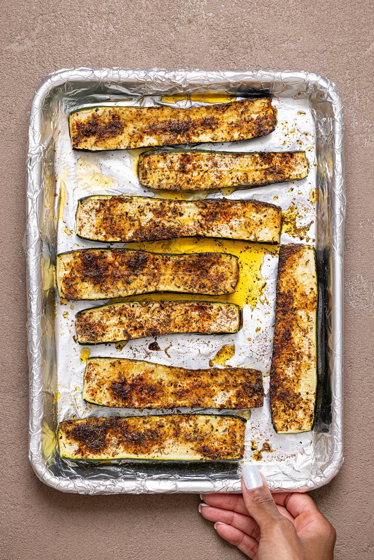 Roasted zucchini being held on a baking sheet with foil paper. 