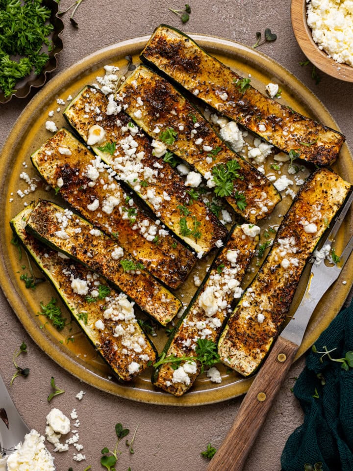 Roasted zucchini on a plate with a fork and feta cheese.