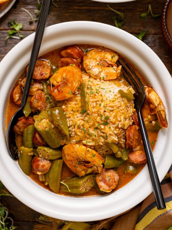 A white bowl with gumbo and a fork + spoon.