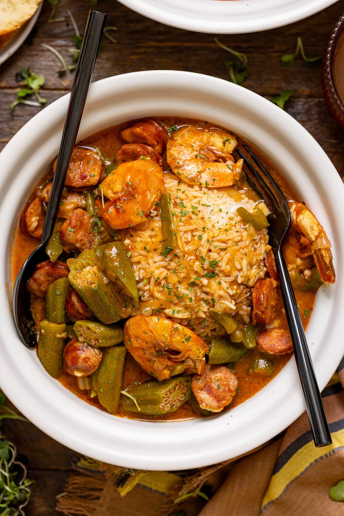 A white bowl with gumbo and a fork + spoon.