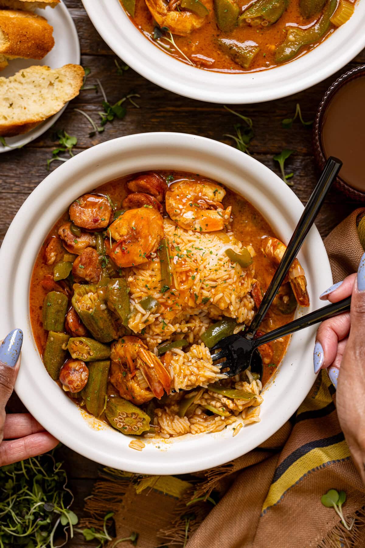 Bowl of gumbo being held with two spoons with a hand.