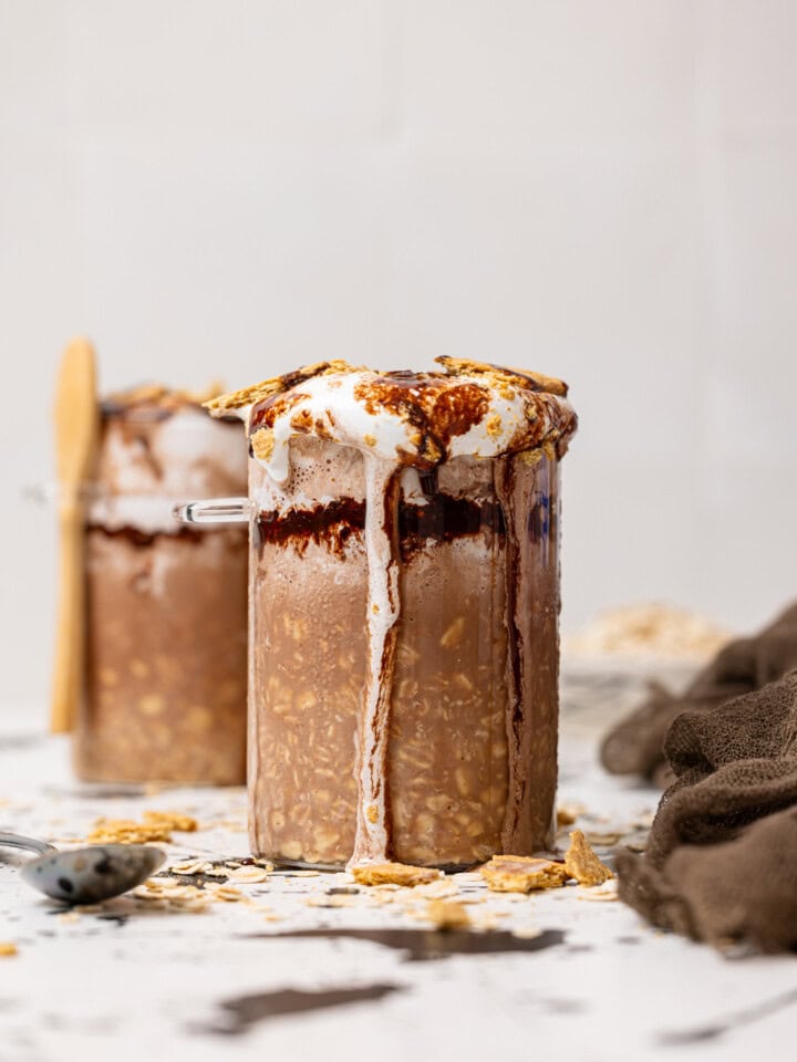 Two jars filled with S'more overnight oats with a spoon and Graham crackers as topping.