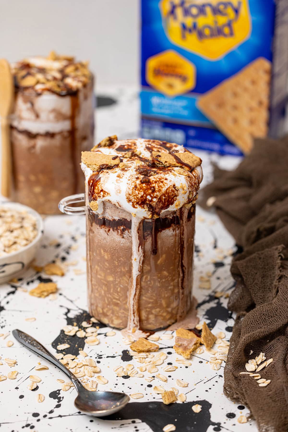 S'Mores overnight oats in two jars with a box of Graham Crackers and a spoon.