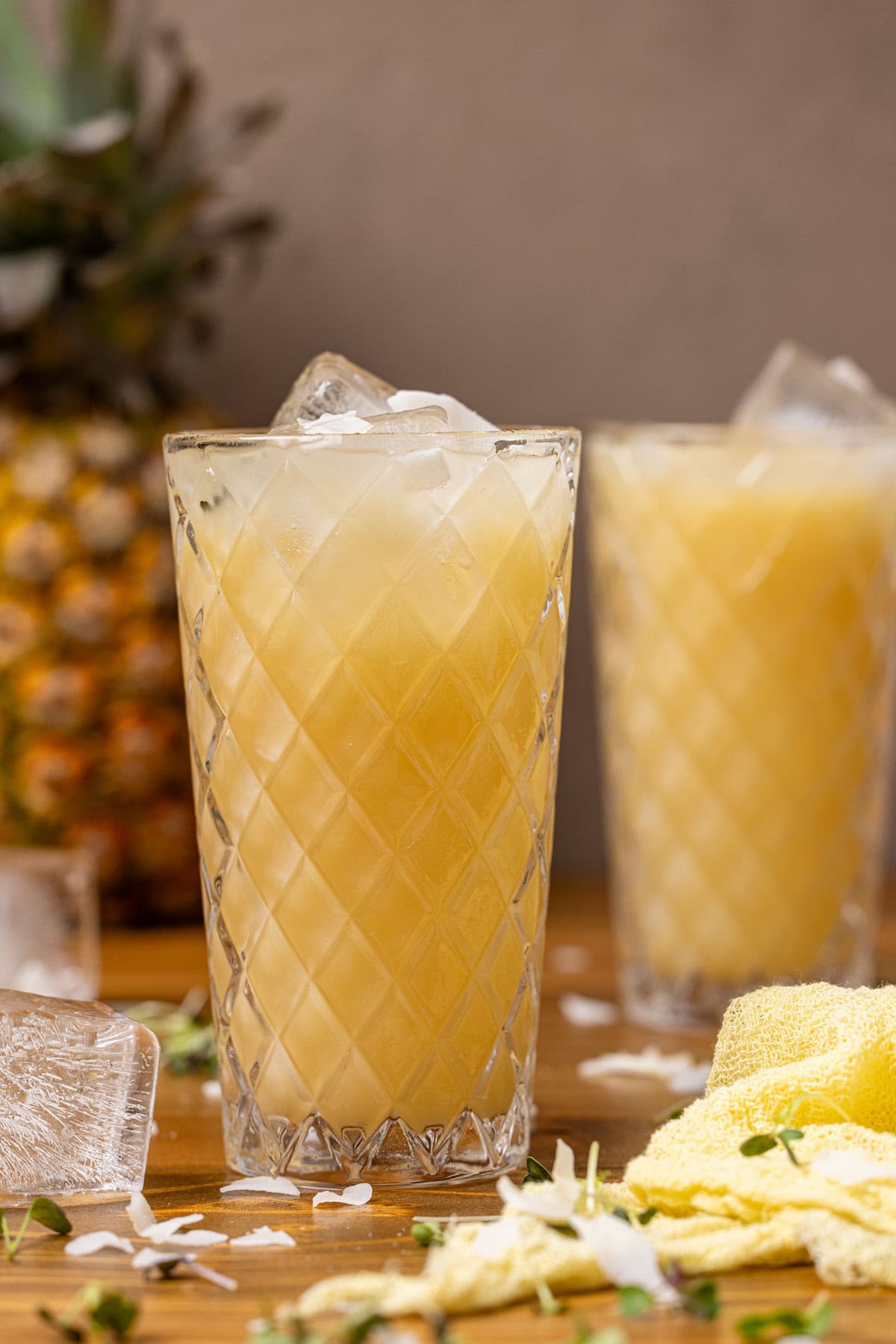 Two glasses on pineapple coconut drink with ice cubes.