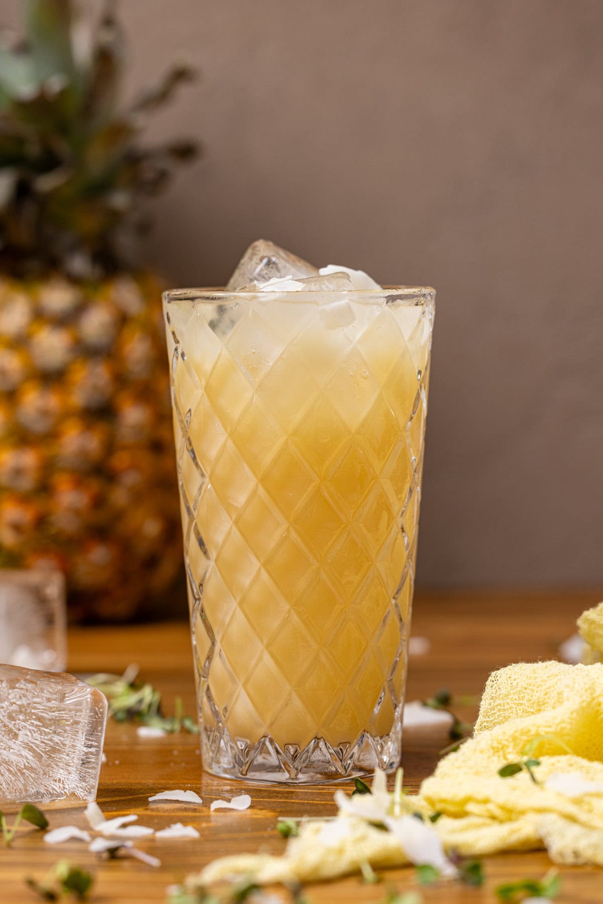 A glass of pineapple coconut drink with a pineapple and ice cubes.