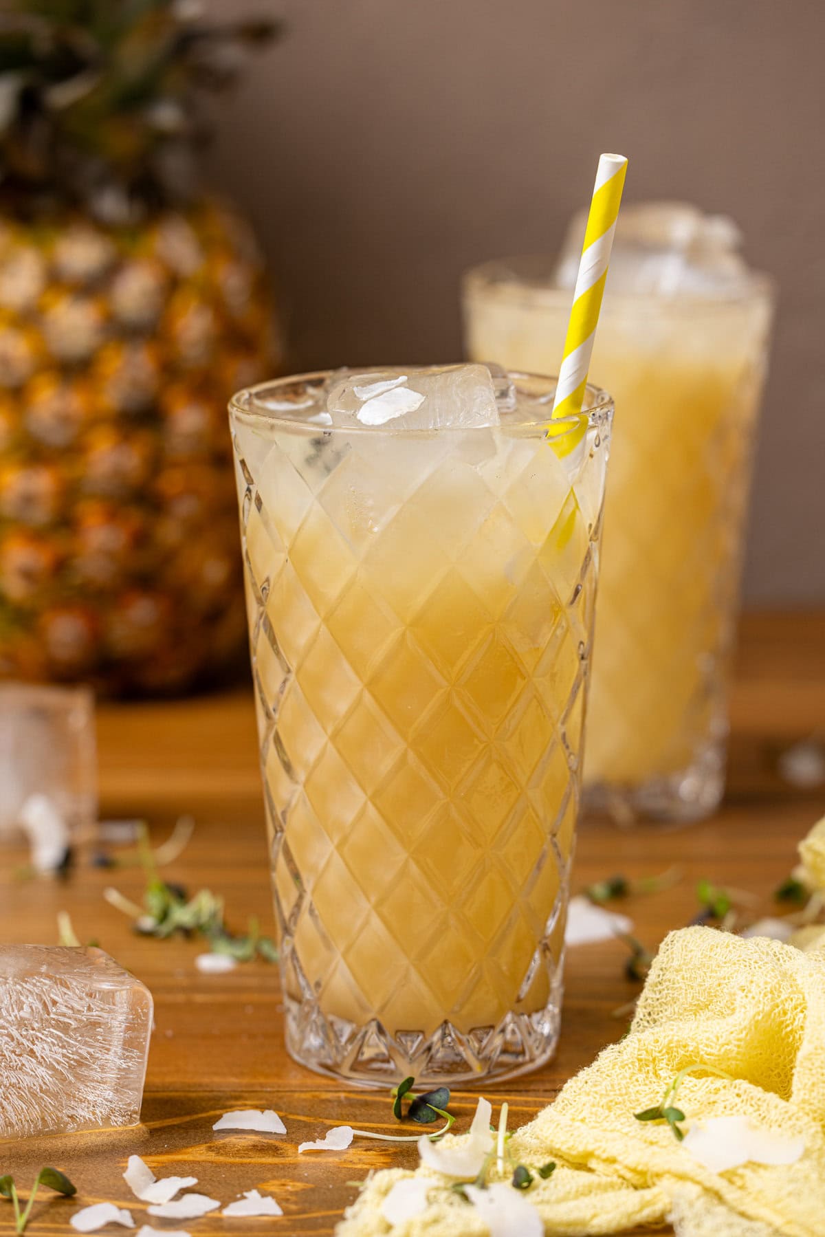 Two glasses of sparkling pineapple coconut drink with a straw.