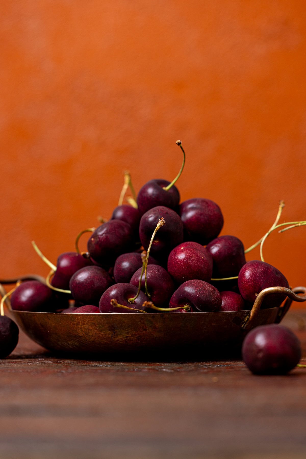 Fresh cherries stacked in a bowl on a burgundy wood table.