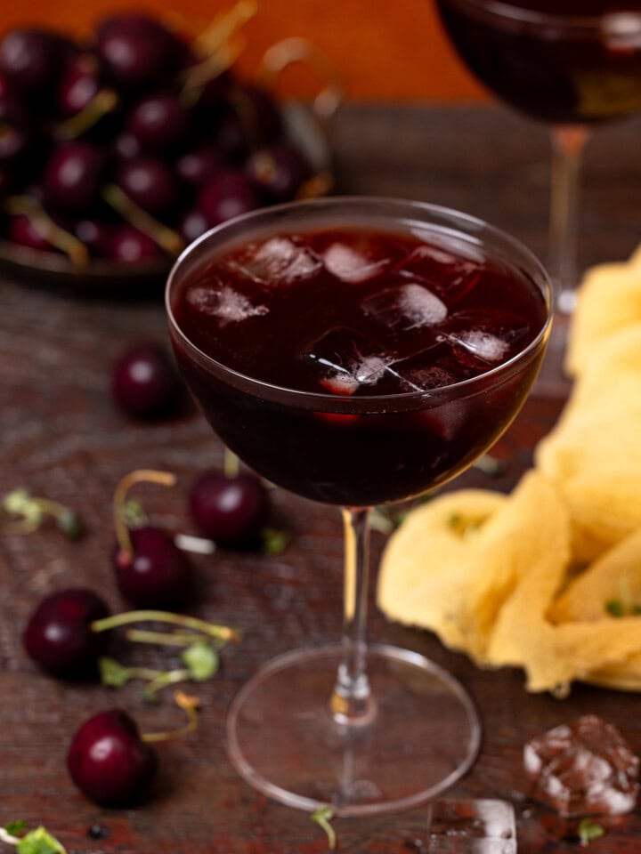 Up close shot of sparkling tart cherry drink in a stem glass with cherries + ice cubes.