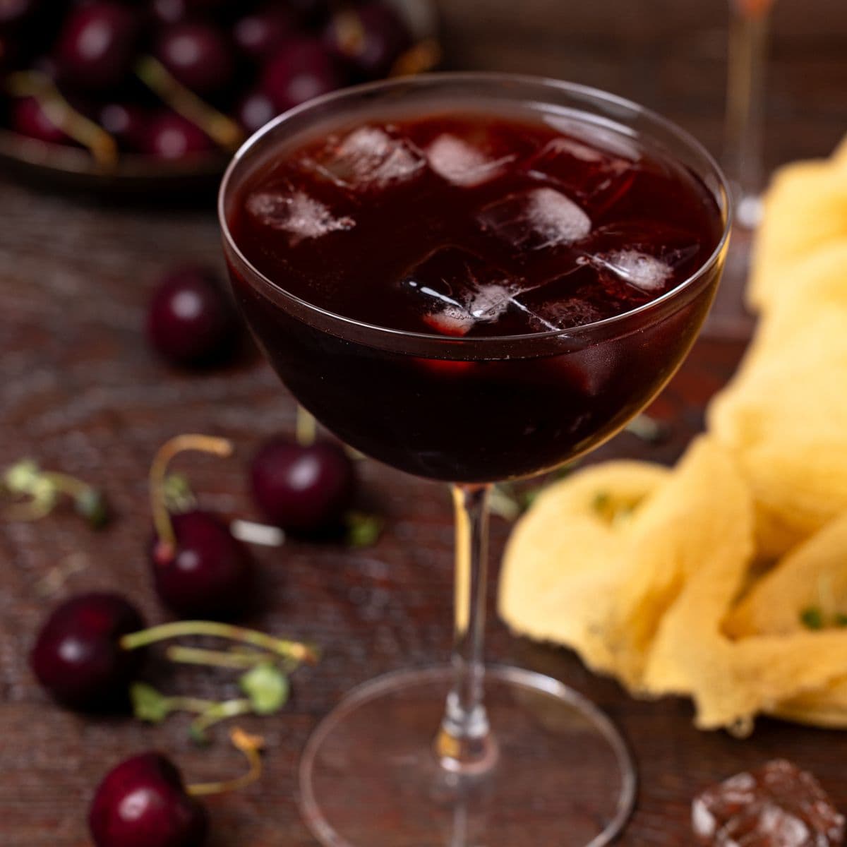 Up close shot of sparkling tart cherry drink in a stem glass with cherries + ice cubes.