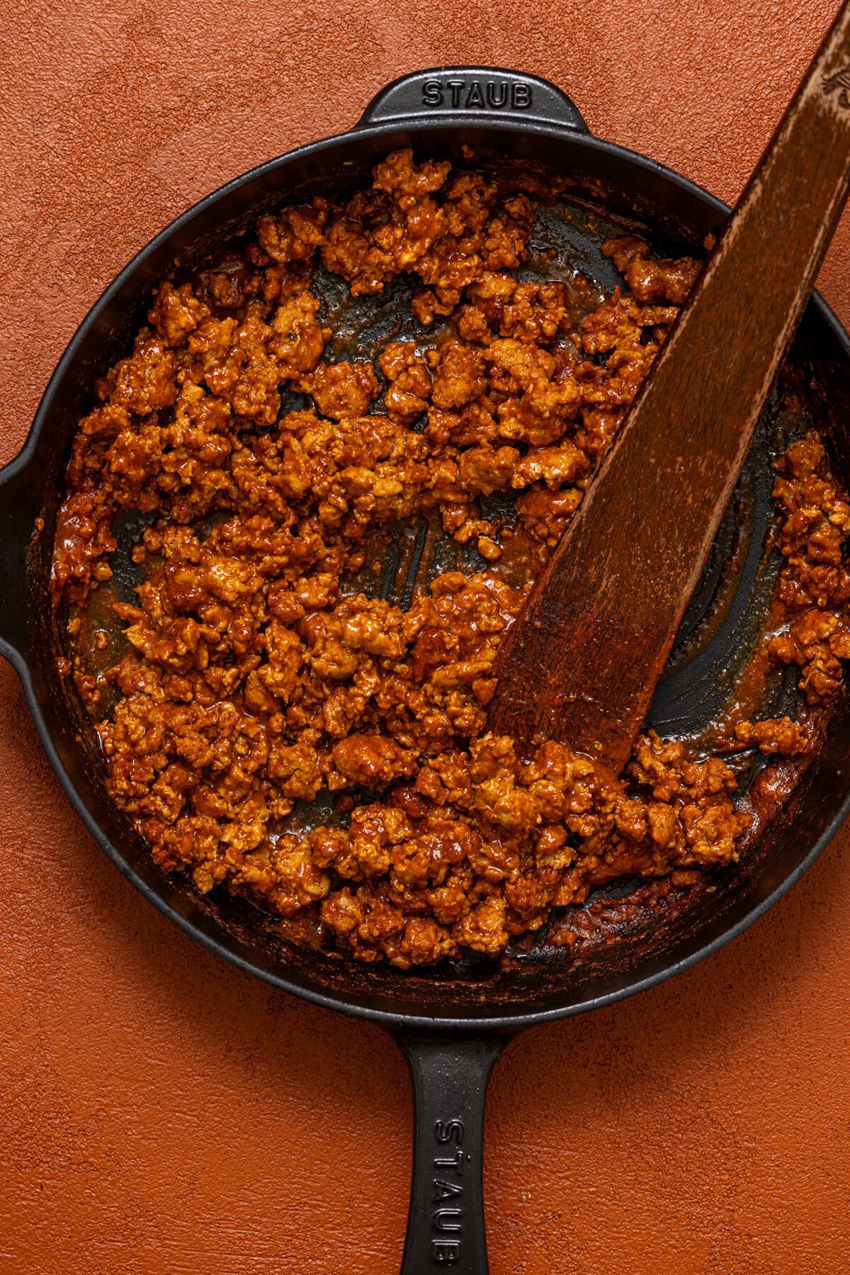 Cooked Al Pastor turkey meat in a skillet with a wooden spoon.