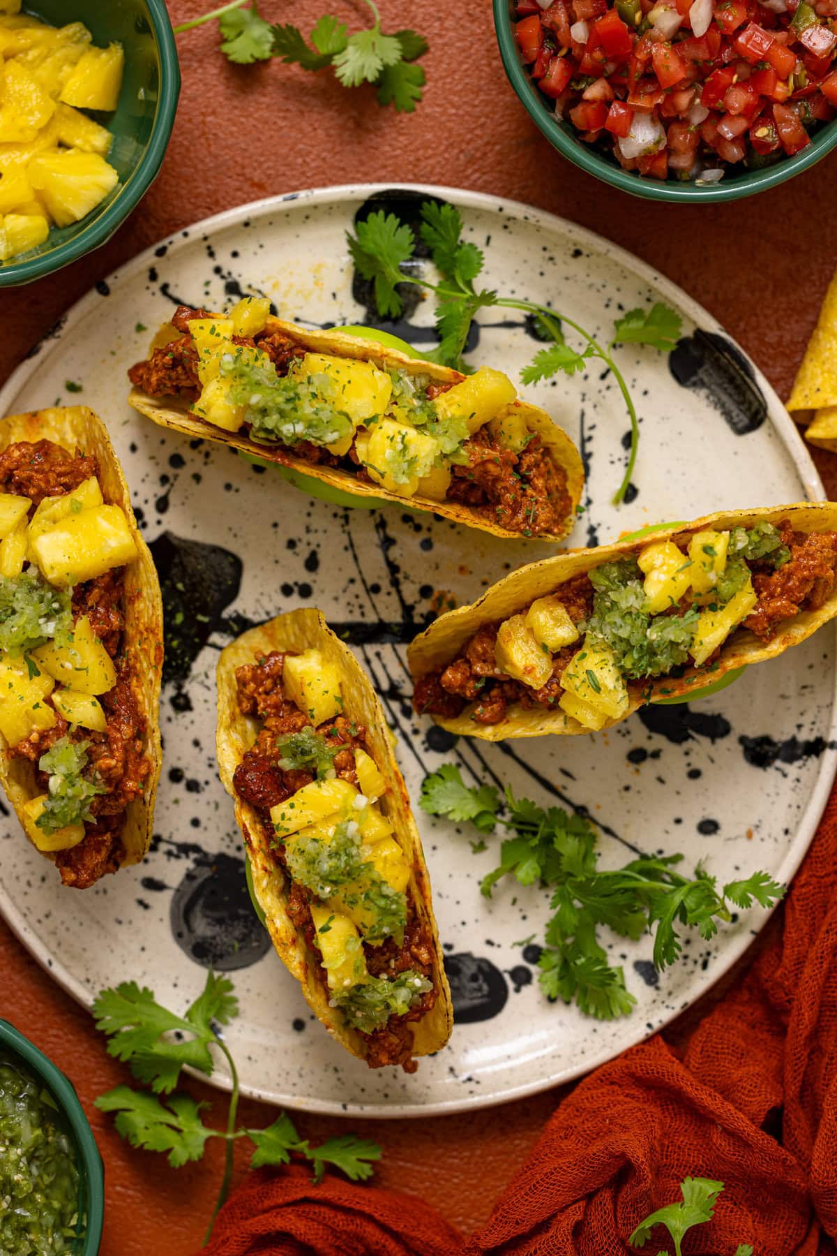 Tacos on a black and white plate with sides of toppings and herb garnish.