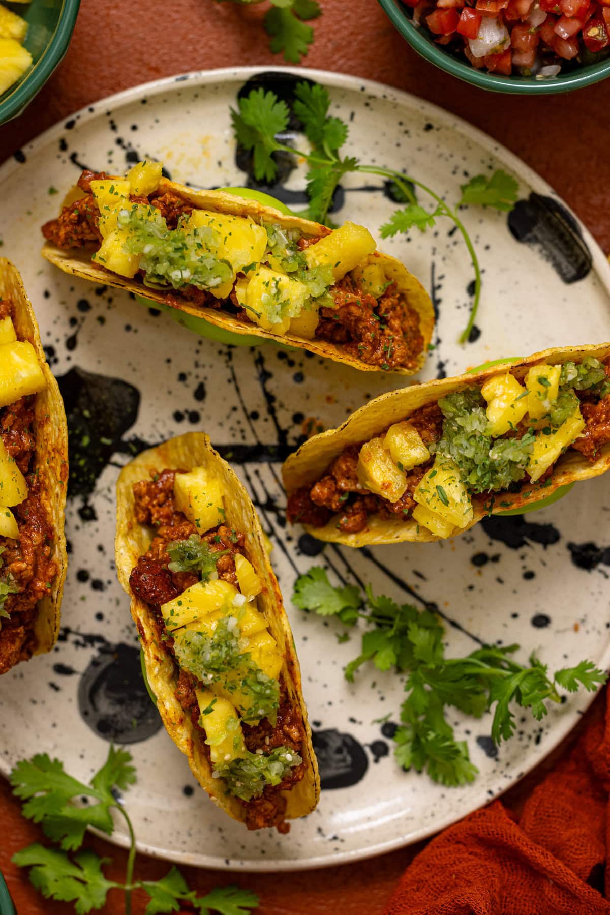 Four tacos on a plate in taco holders with herb garnish.