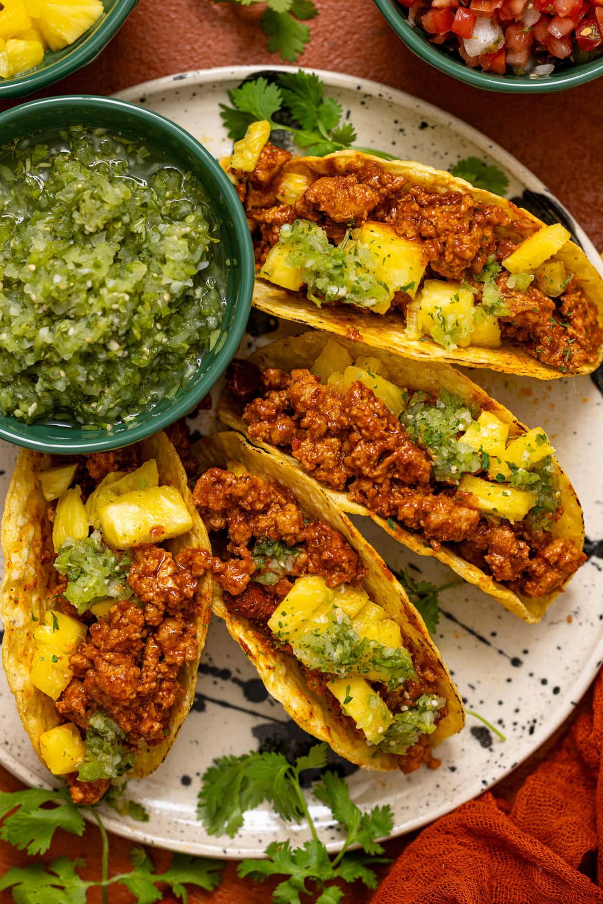 Tacos lined on a plate with verde salsa and herb garnish.