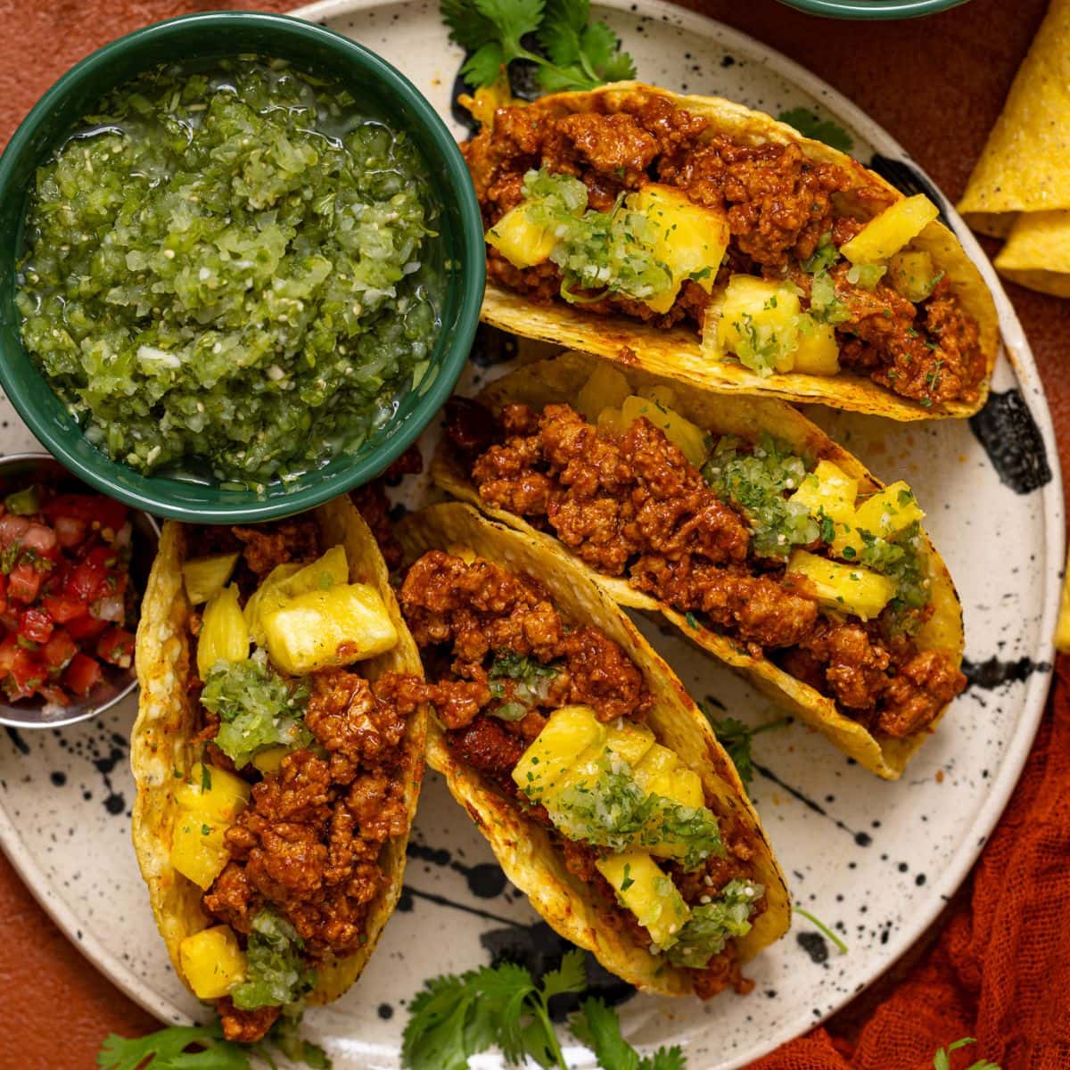 Tacos lined on a plate with verde salsa and sides of toppings.