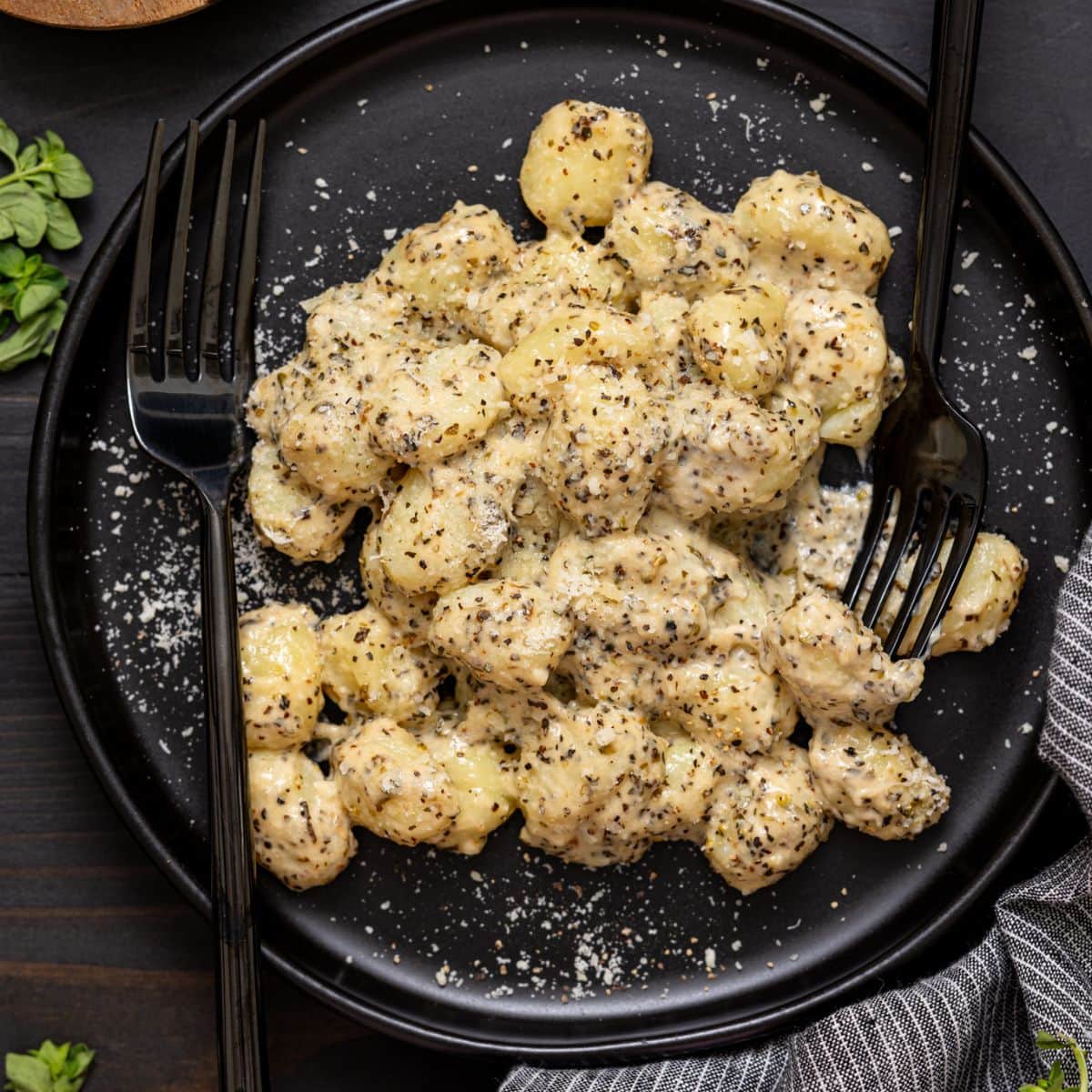 Up close shot of gnocchi on a black plate with two forks and grated parmesan.