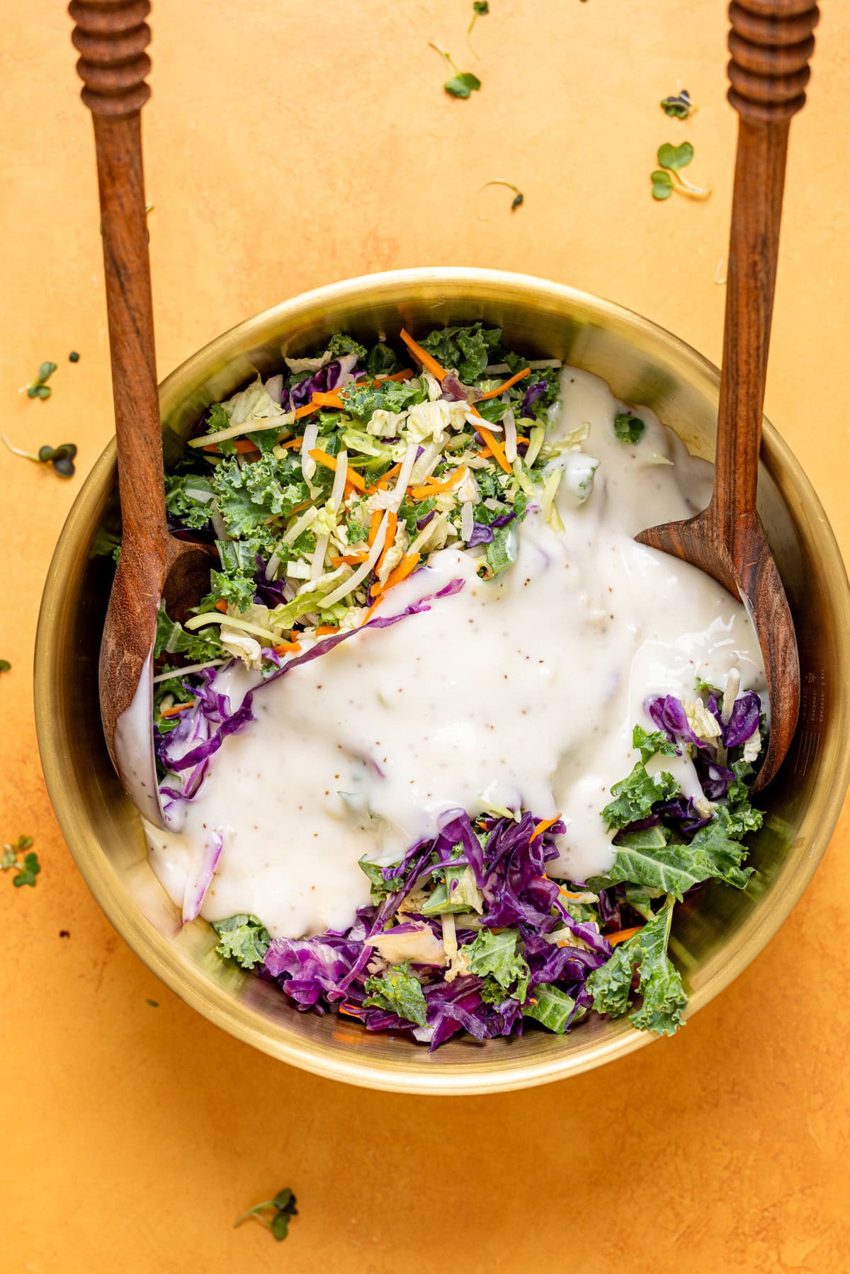 Coleslaw ingredients in a gold bowl with two wooden spoons.