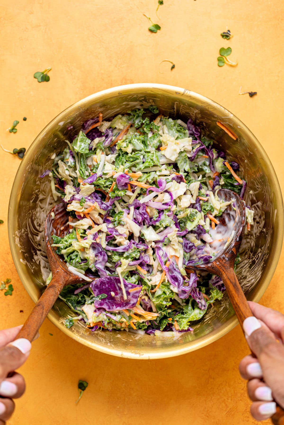 Coleslaw ingredients being stirred together in a gold bowl.