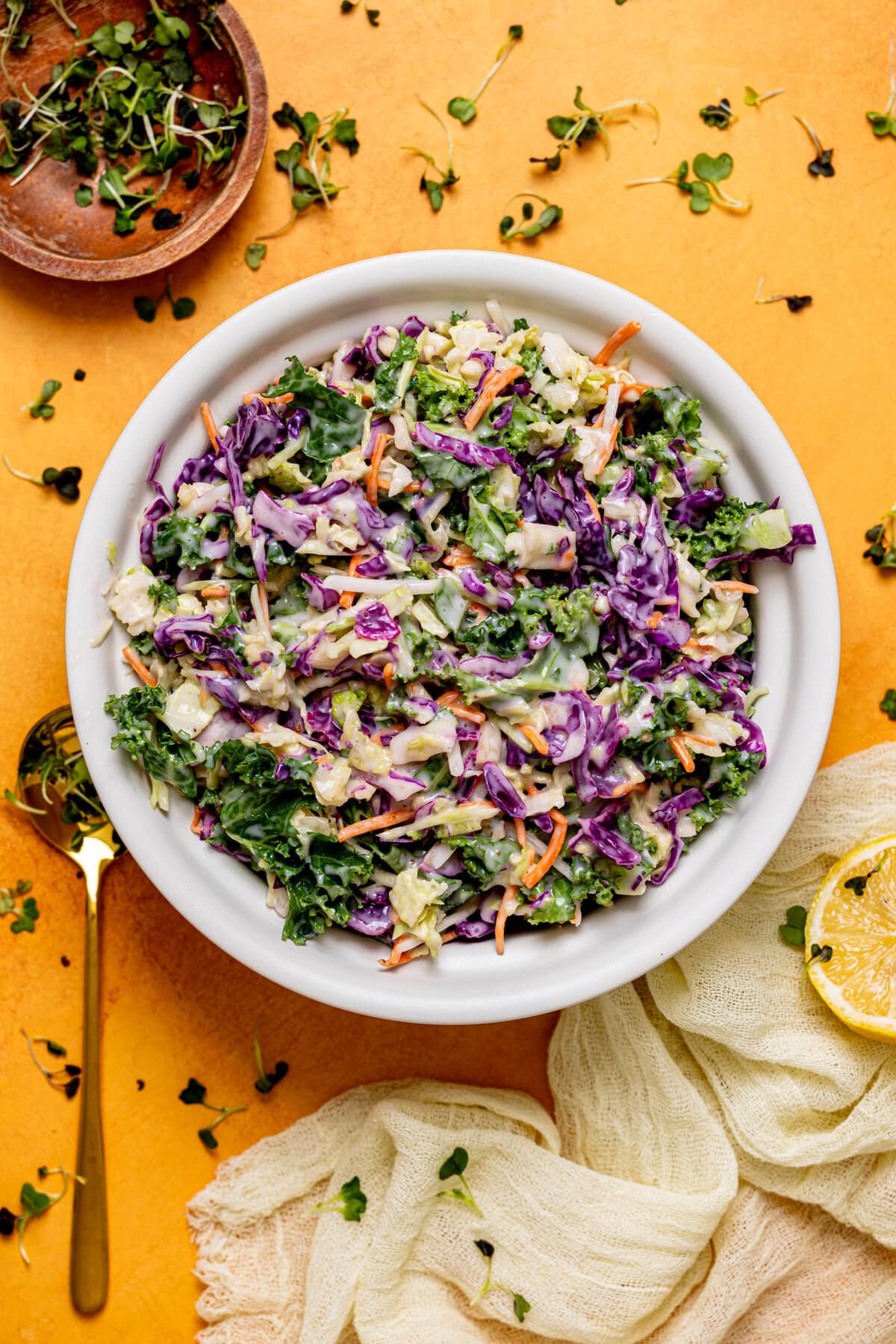 Coleslaw in a white bowl with a spoon on a yellow table. 