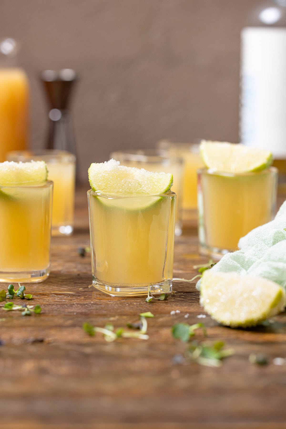 Green tea shots lined up on a brown wood table with lime wedges.