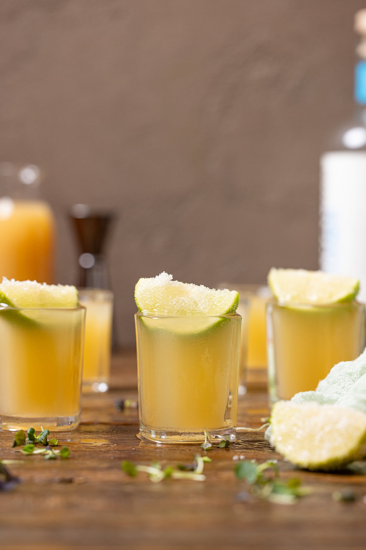 Green tea shots with lime wedges and alcohol alternative in the background.