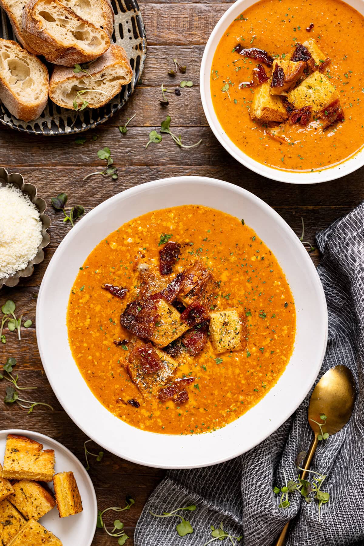 Two bowls of tomato bisque with a side of bread and grated parmesan.