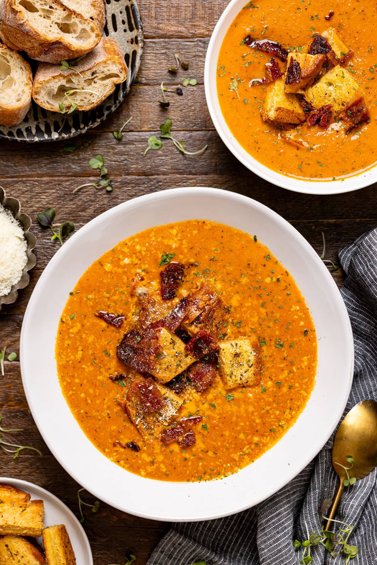 Two bowls of tomato bisque with a spoon and a side of bread.