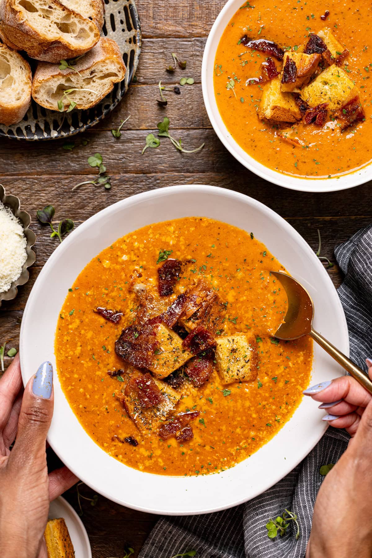 Two bowls of tomato bisque with a spoon and bowl being held.