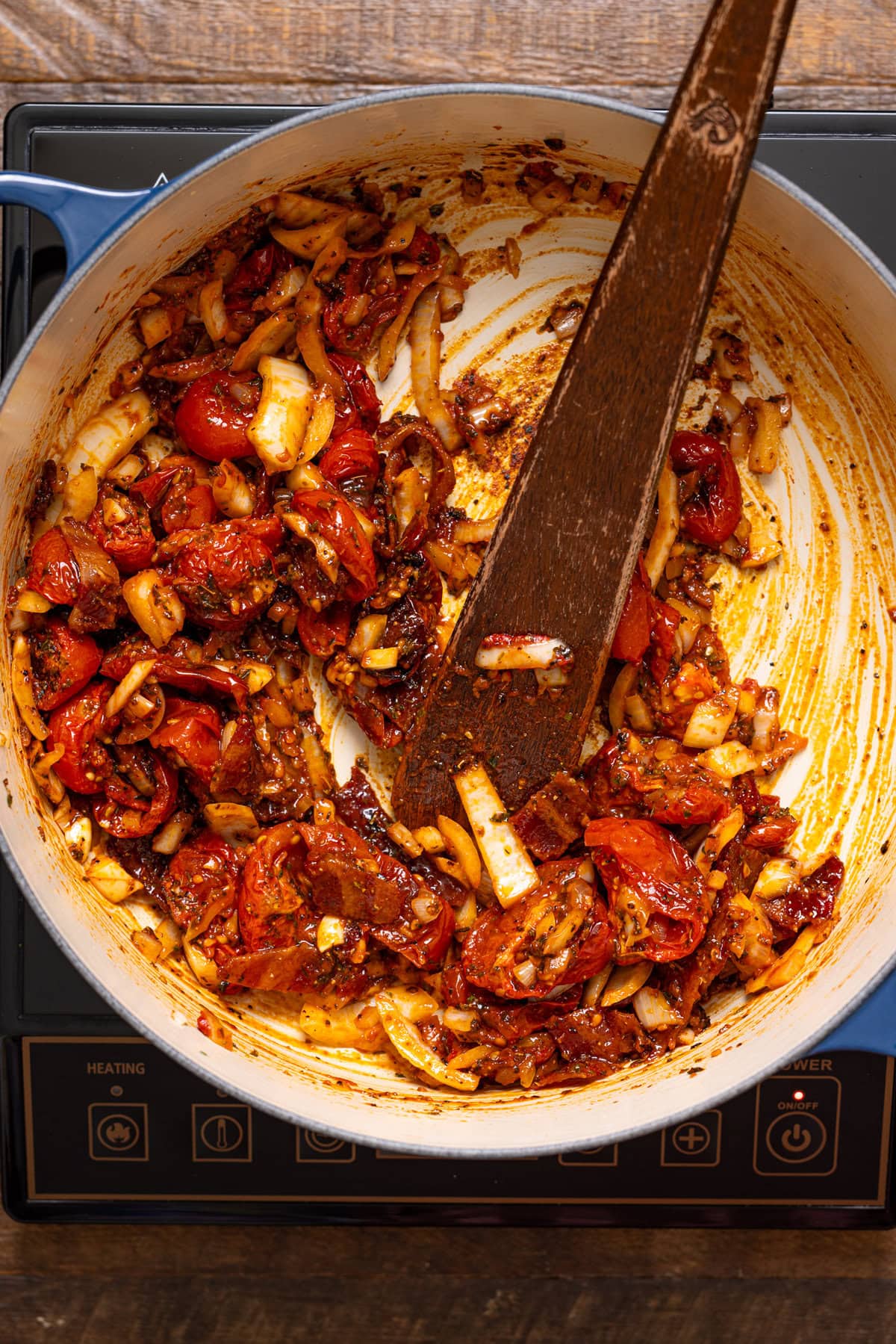 Sautéed veggies and tomatoes in a pot with a wooden spoon.