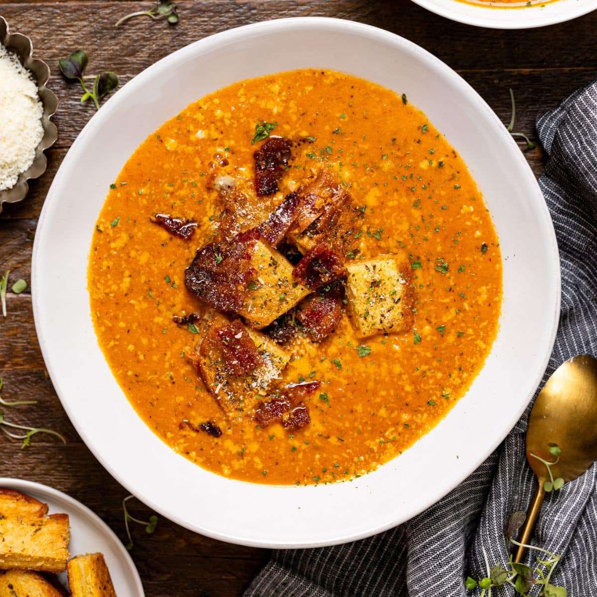 Two bowls of tomato bisque with a spoon and a side of bread.