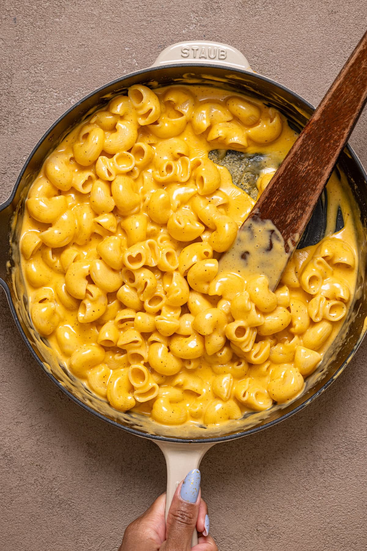 Mac and Cheese in a skillet being held with a wooden spoon.