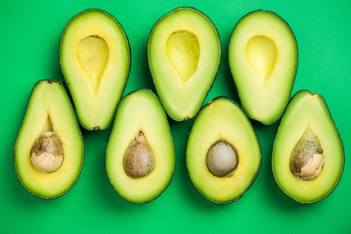 Avocados cut in half on green background.