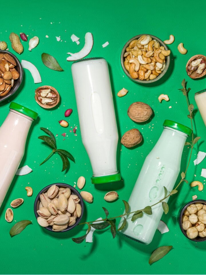 Milk bottles, nuts, seeds and herbs on bright green backdrop.