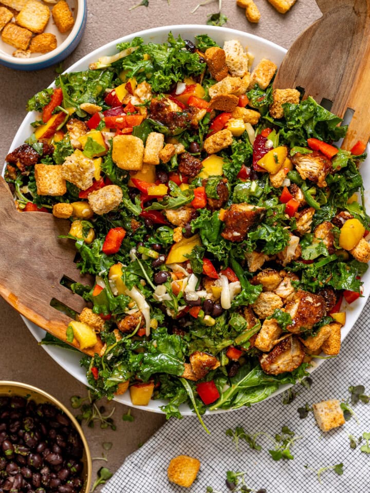 BBQ Chicken Peach Chopped Salad in a serving bowl with wooden serving spoons and toppings on the side.