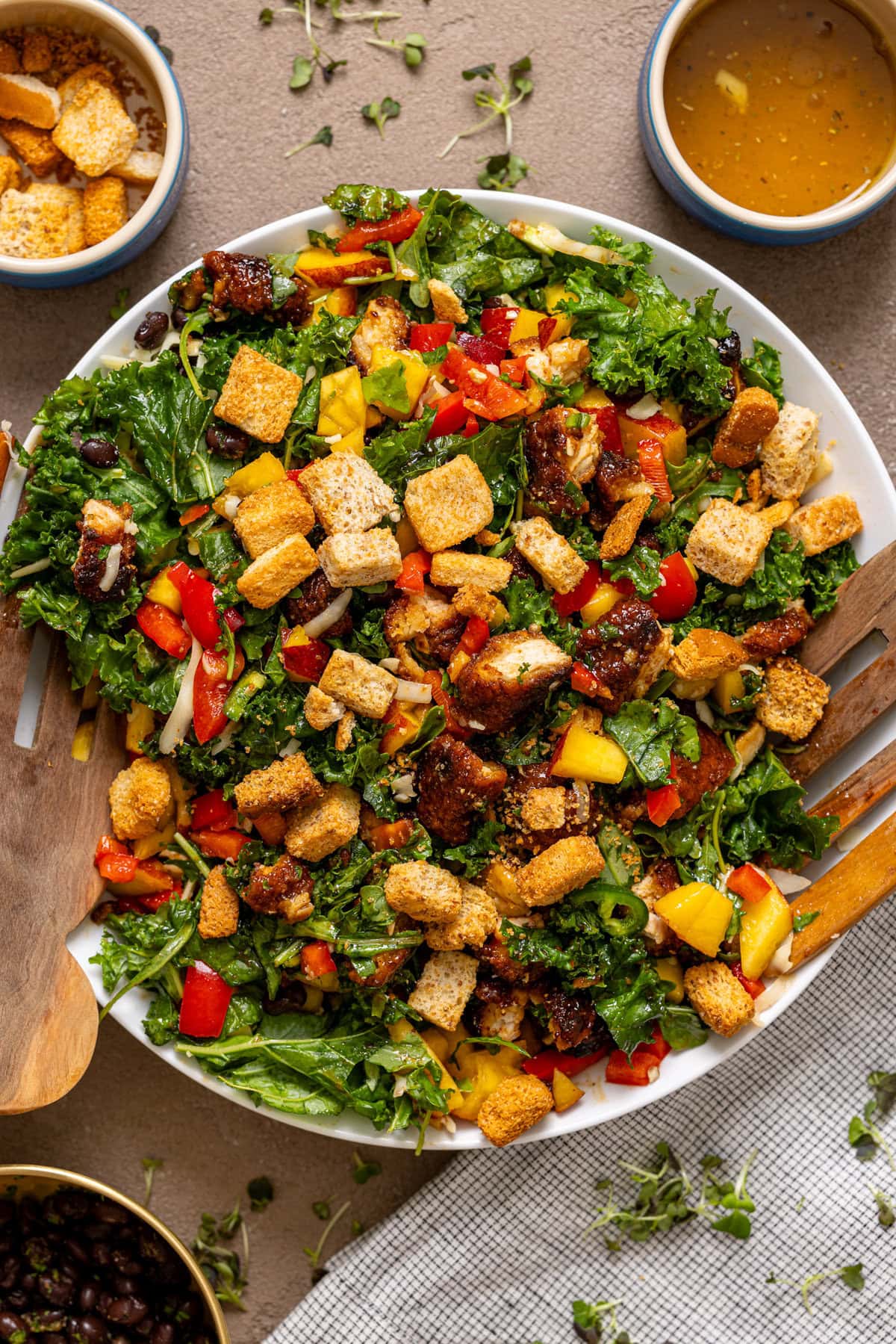 BBQ Chicken Peach Chopped Salad in a serving bowl with wooden serving spoons and a side of dressing.