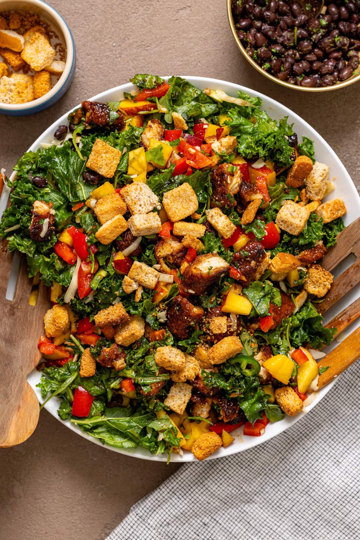 Chicken salad in a serving bowl with wooden serving spoons and ingredients on the side.