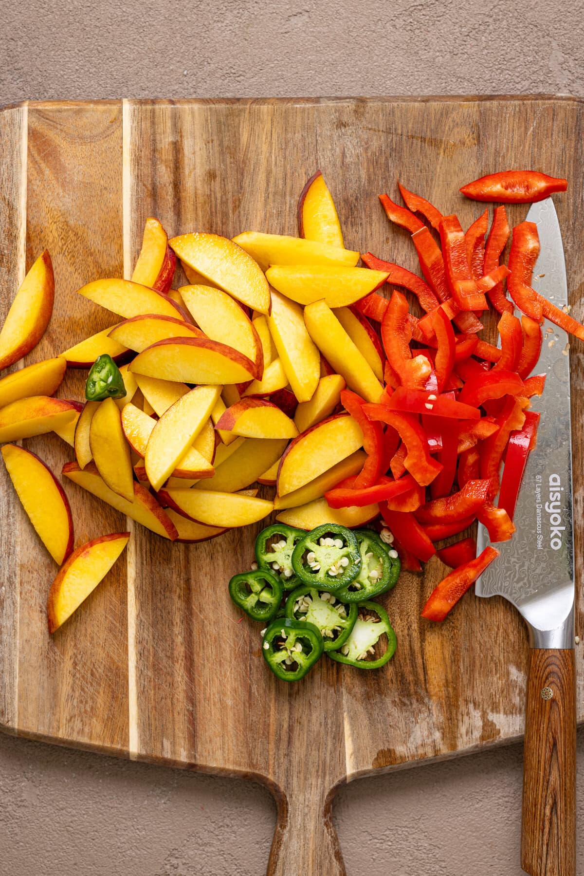 Chopped peaches + veggies on a cutting board with a knife.