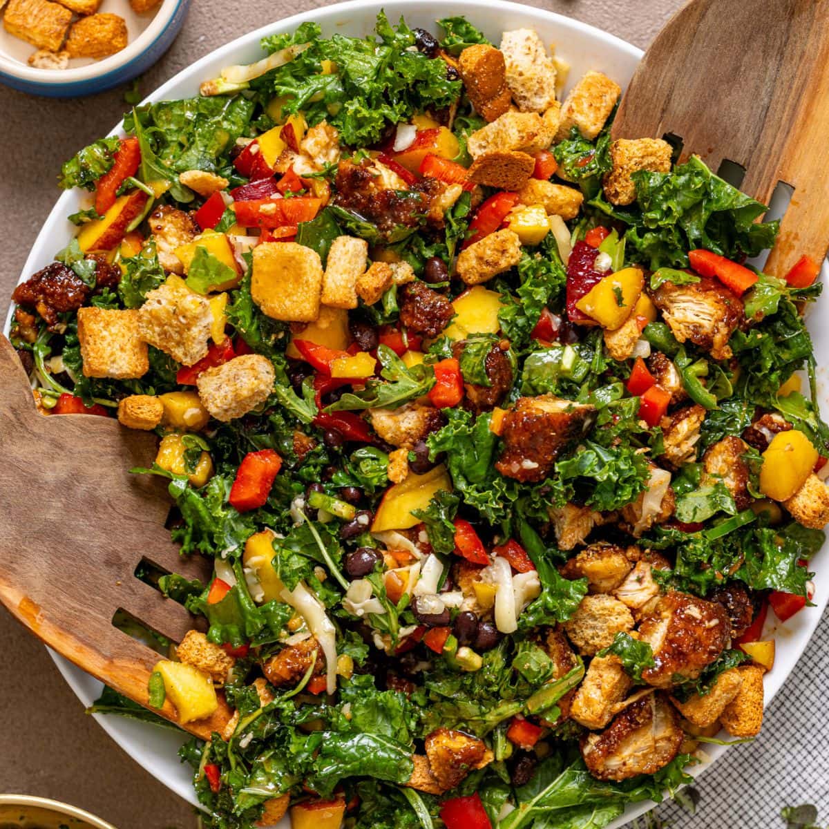 BBQ Chicken Peach Chopped Salad in a serving bowl with wooden serving spoons and toppings on the side.